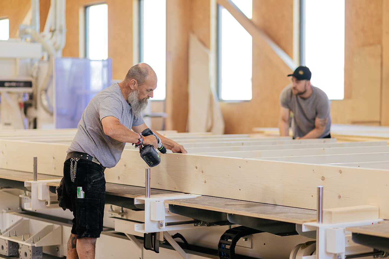 Präzise Handarbeit im Holzbau bei Aischtaler Holzhaus Holzbau-Handwerker von Aischtaler Holzhaus verschrauben Holzelemente in der Werkhalle